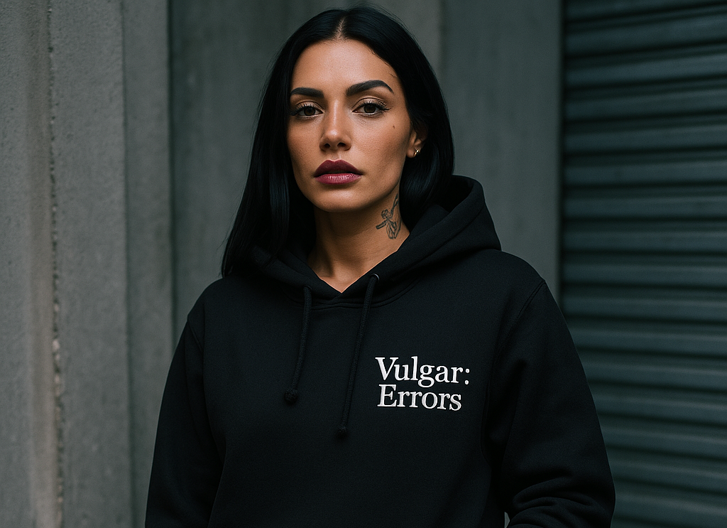 Person wearing a black hoodie with 'Vulgar: Errors' text against a gray wall.